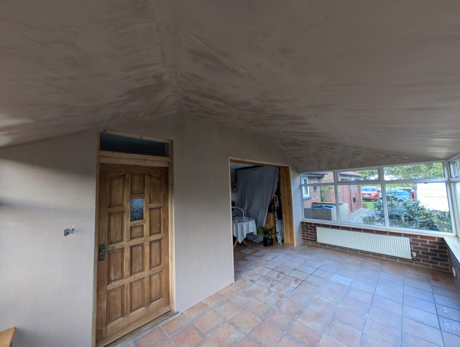 Plastered walls and ceiling around a wooden door, windows beyond