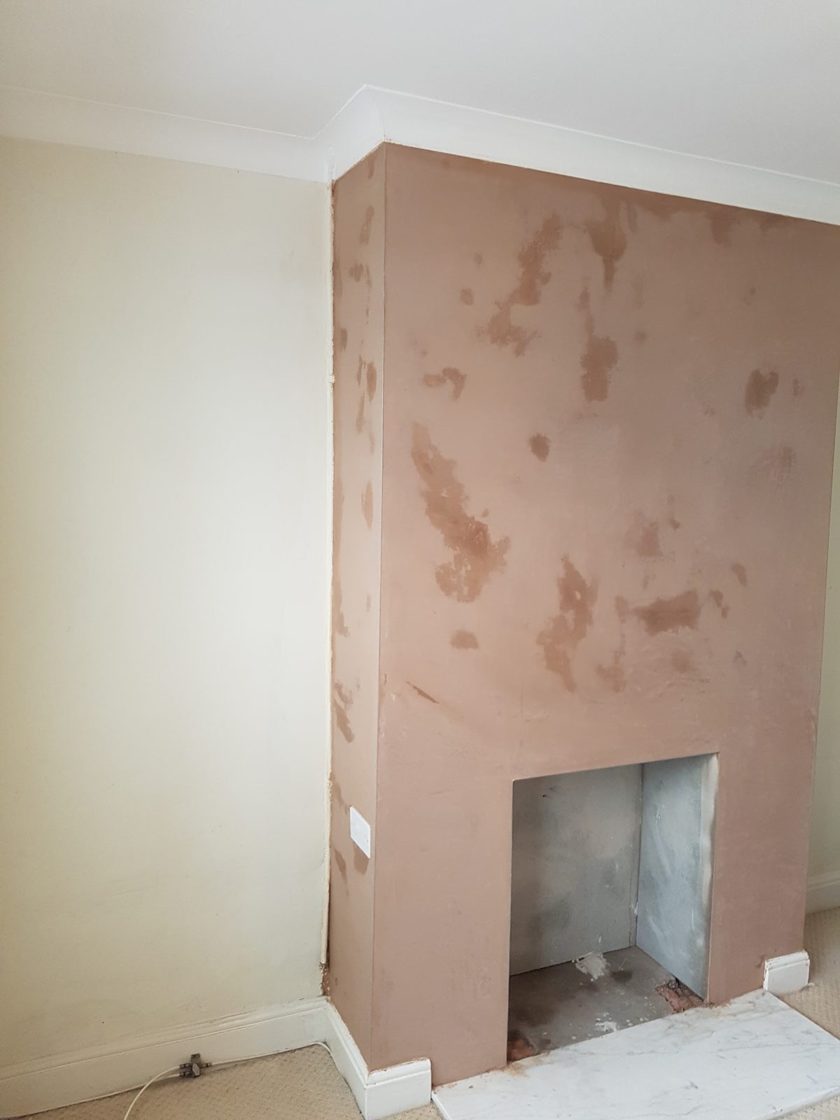 Chimney breast freshly replastered, patches still drying, fireplace opening below