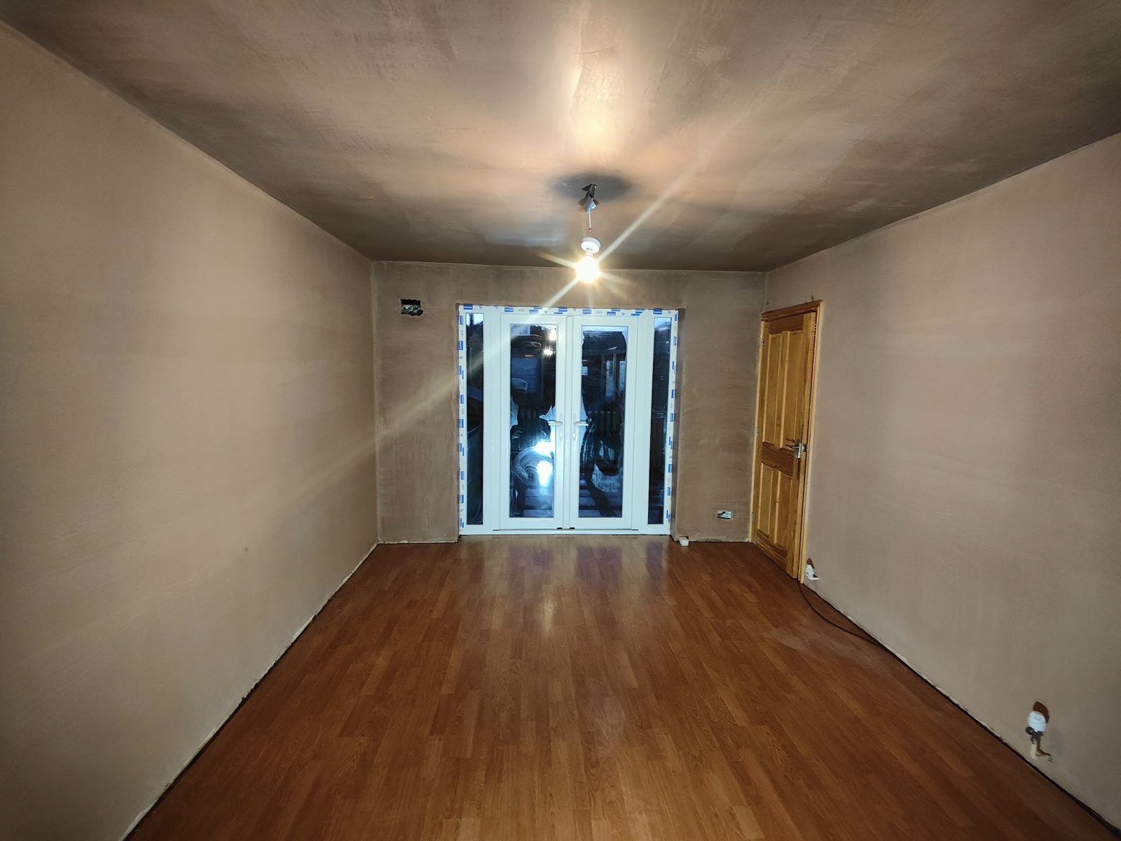 Lounge with smooth new plaster on every wall, French doors at the far end
