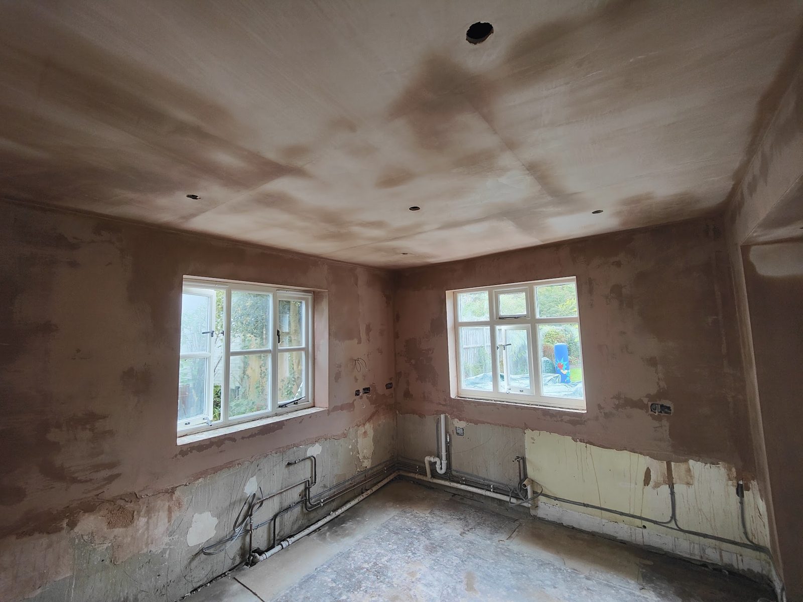 Kitchen stripped back with walls and ceiling replastered, pipework still exposed