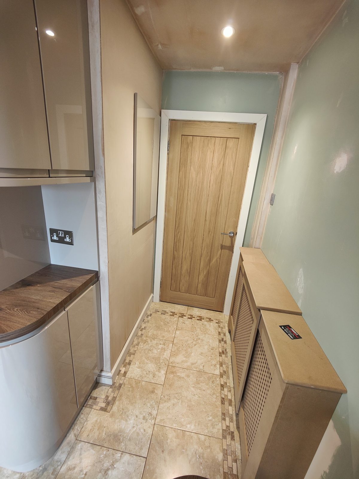 Galley kitchen with gloss units and an oak door, walls freshly plastered