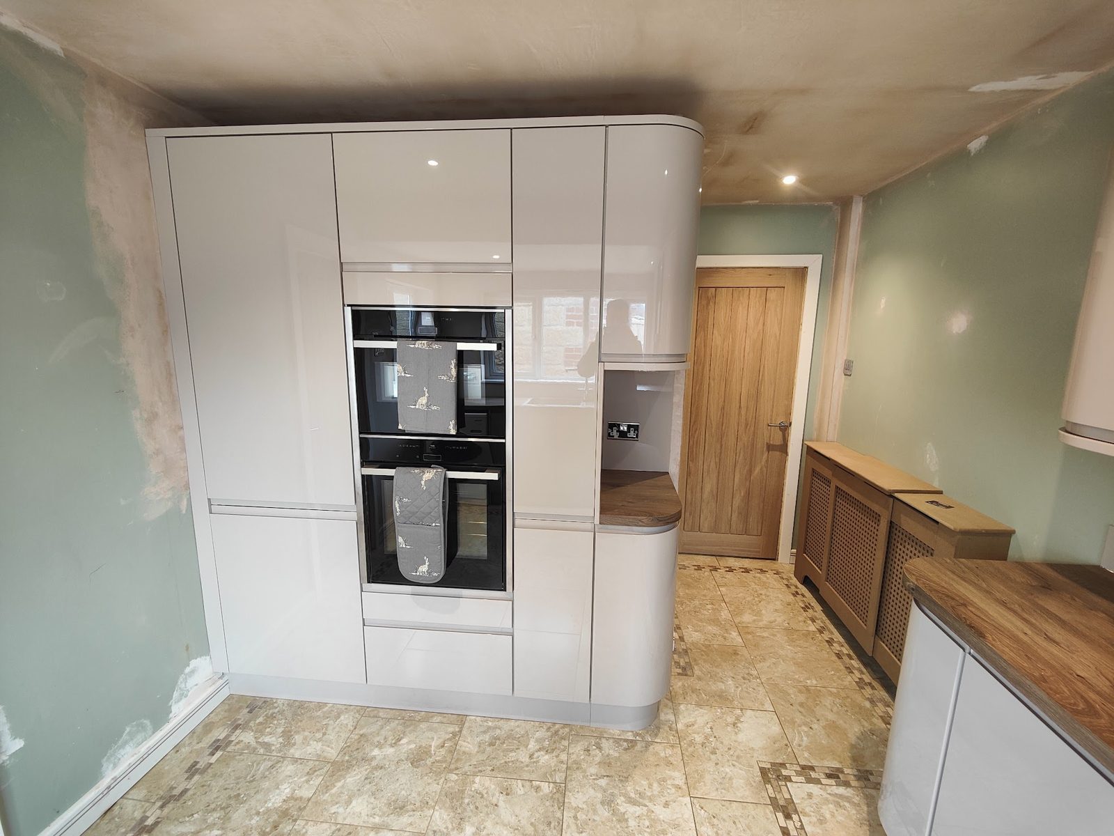 Tall oven housing in a cream gloss kitchen, plaster still drying on the wall